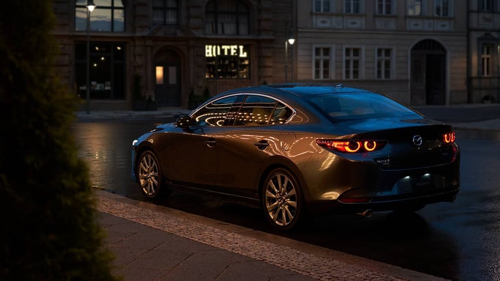 The 2023 Mazda3 Sedan sitting on a well-lit street in the evening to showcase the back view of the exterior